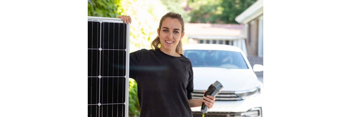 Portrait of young woman holding a solar panel showing the source of energy for her electric white car and a plug on hand