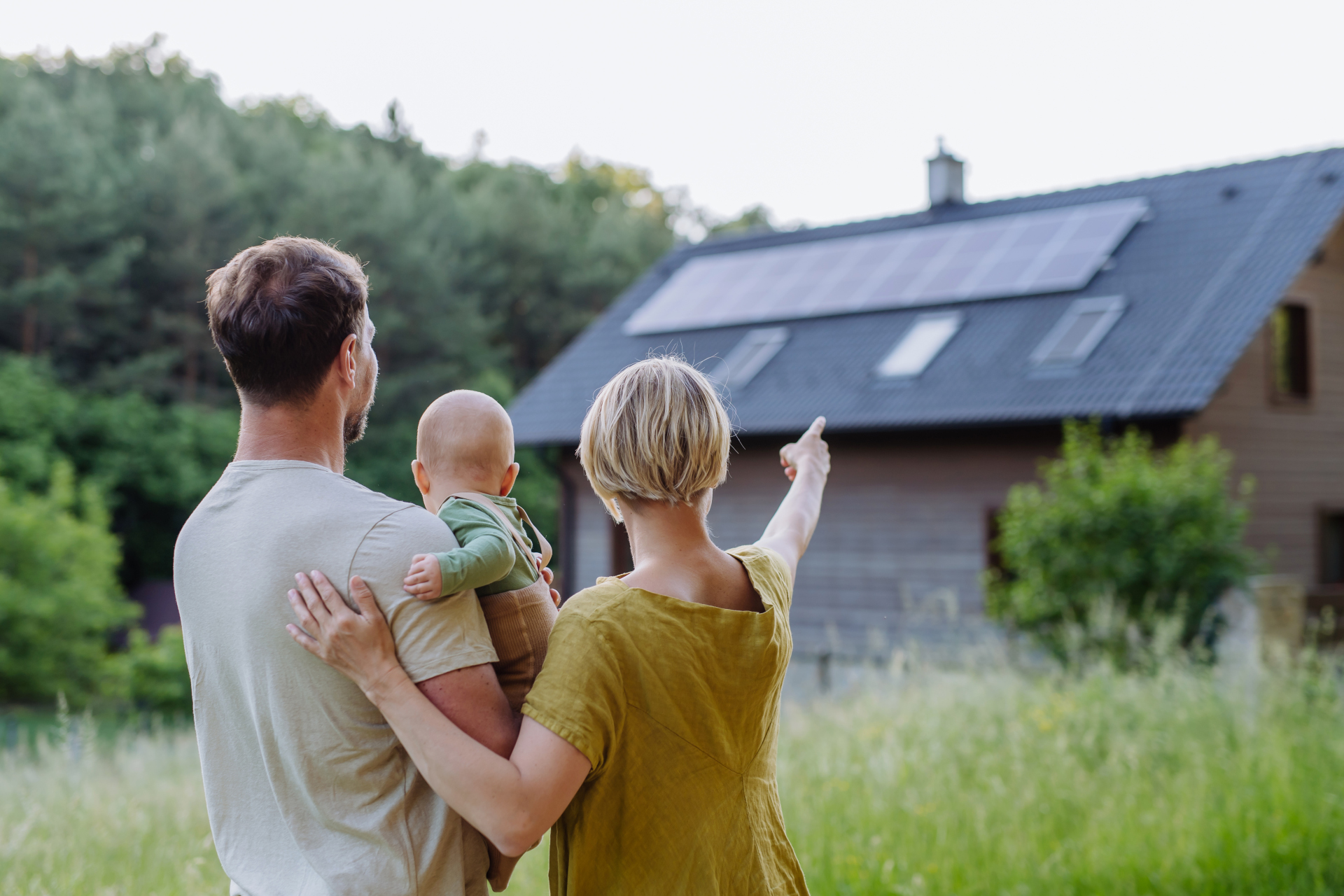 Rear view of family near their house with solar panels. Alternative energy, saving resources and sustainable lifestyle concept.